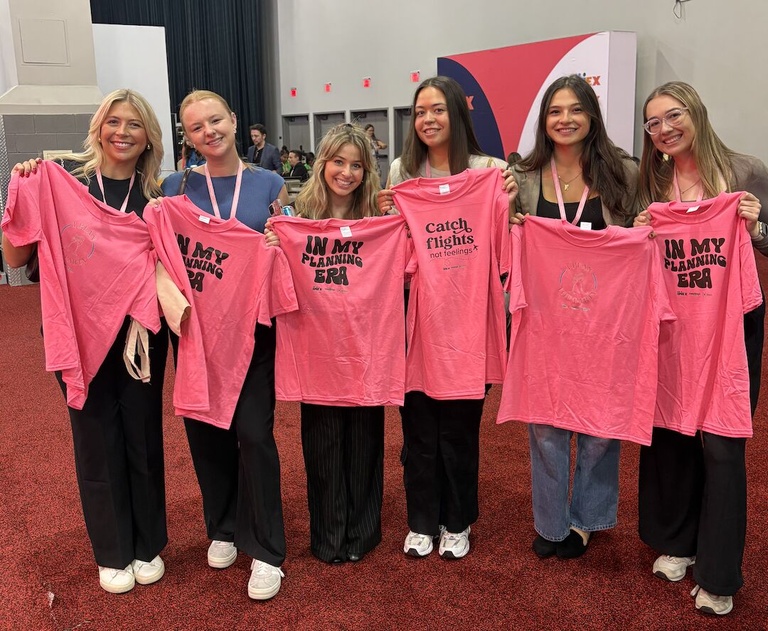 Six seniors holding up pink themed shirts from the imex conference 