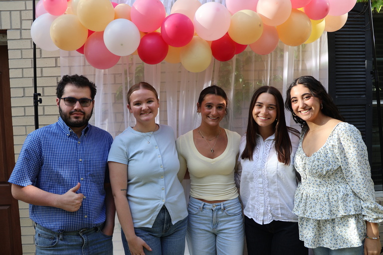 The Spring Graduation workshop group posing for a photo in front of a white backdrop and balloons