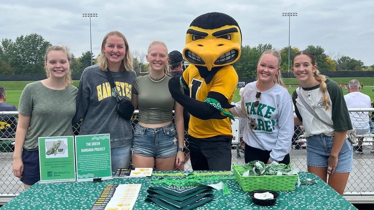 Five students with Herky at an Iowa sporting event tabling for Green Bandanas